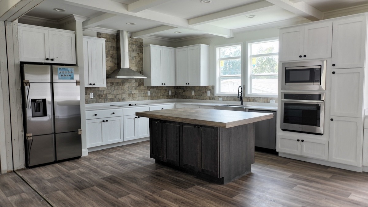 Spacious modern kitchen with white cabinets, stainless steel fridge and oven. Features a dark wood island, stone backsplash, and large windows.