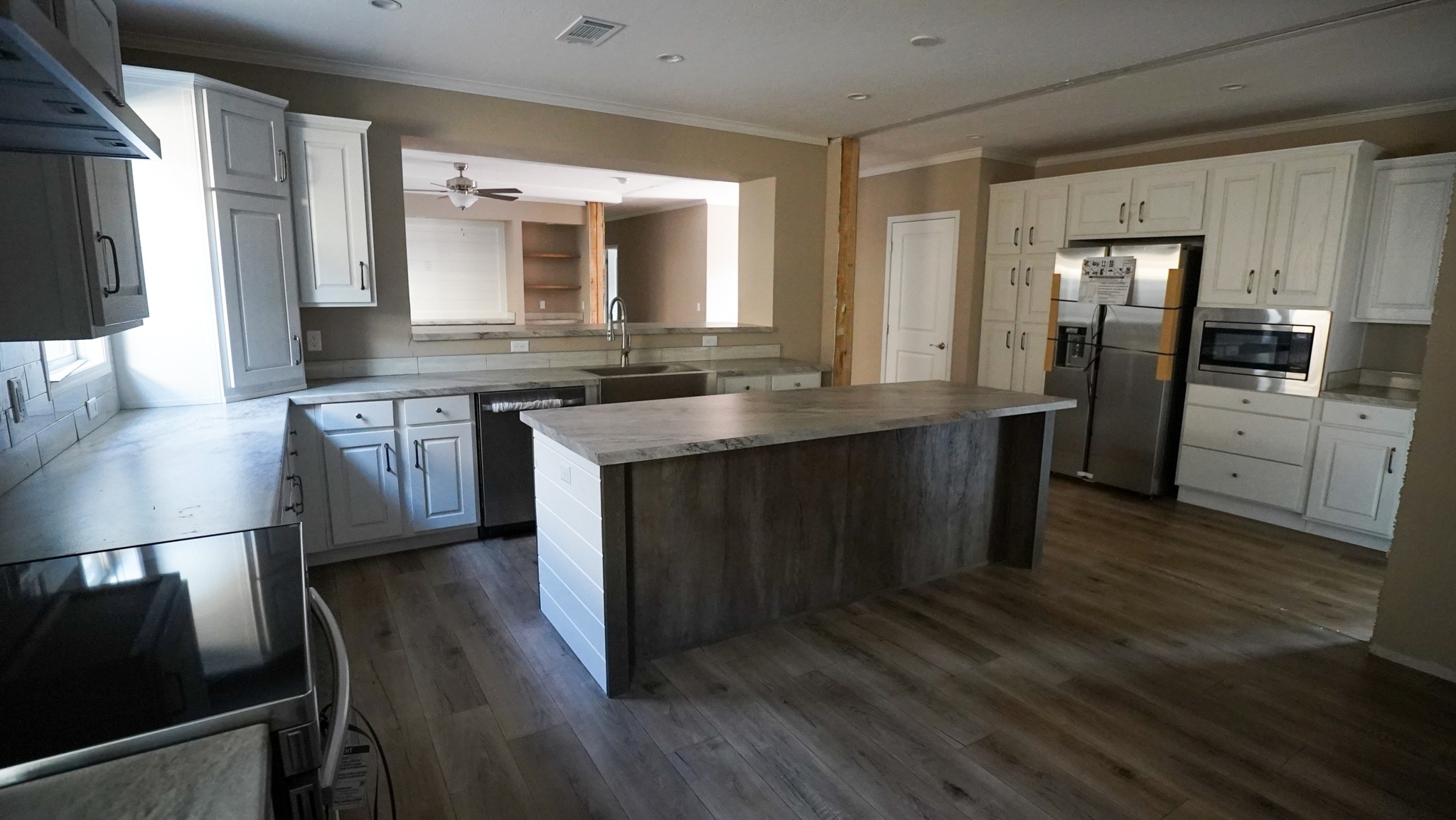Spacious kitchen with white cabinets, stainless steel appliances, and a large wooden island. Natural light from windows creates a warm, inviting ambiance.