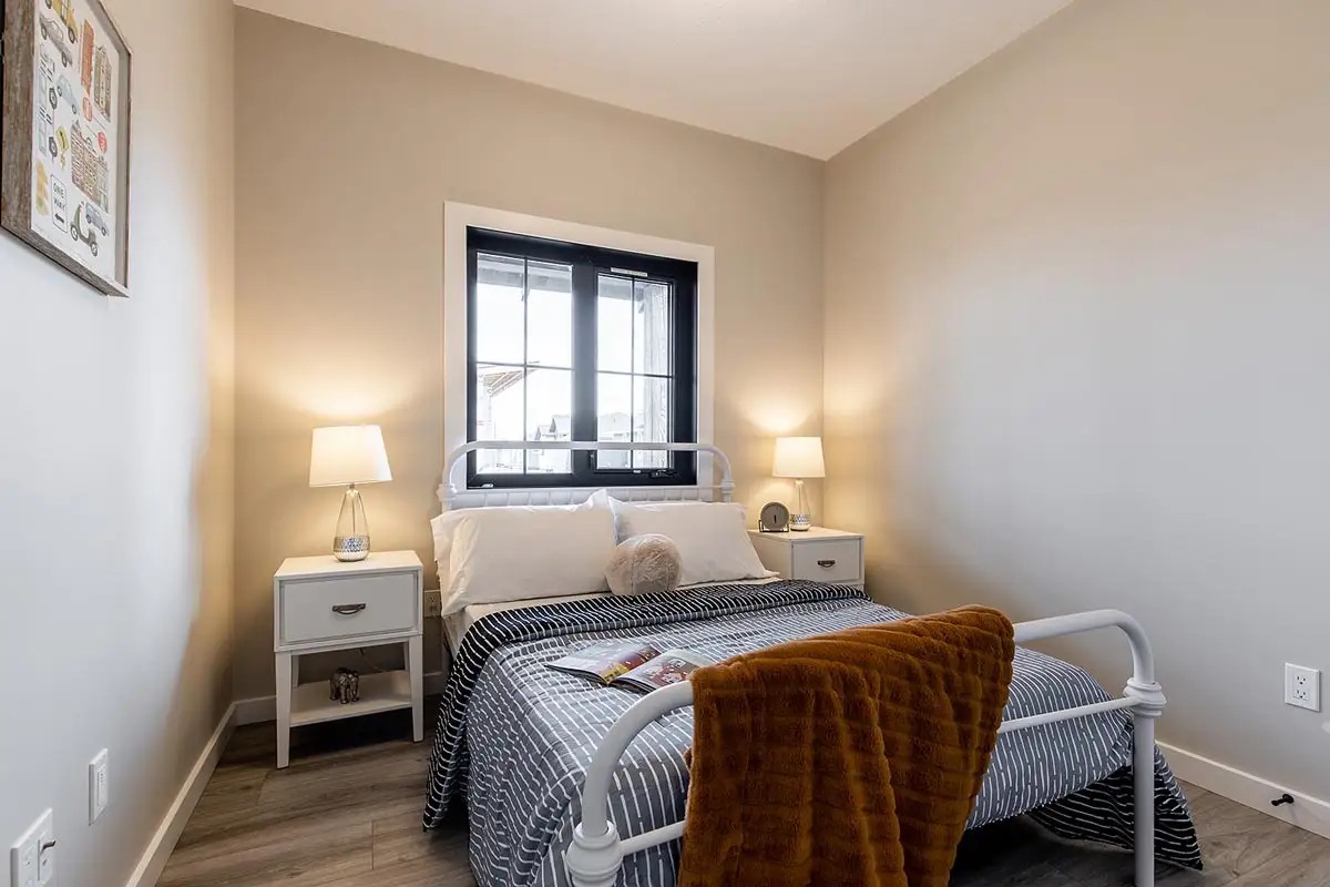 Luxury modern modular home showcase of the APH 1662C 819 SQ FT show home, featuring a white vertical board and batten farmhouse exterior with a metal gabled roof, an open-concept living room with a stacked stone fireplace and vaulted shiplap ceilings, a gourmet kitchen with a granite waterfall island and black industrial pendant lighting, custom floor-to-ceiling pantry storage with pull-out drawers, and a stylish master bedroom with a white iron bed frame and dark-trimmed windows.