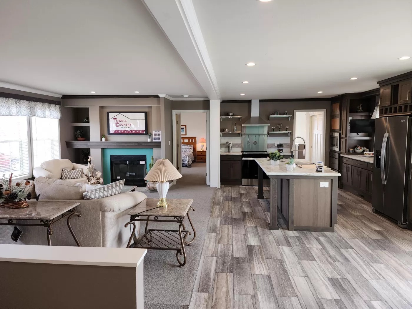 Modern open-concept living room and kitchen with neutral tones. Features a cozy seating area, fireplace, large island, and stainless steel appliances.