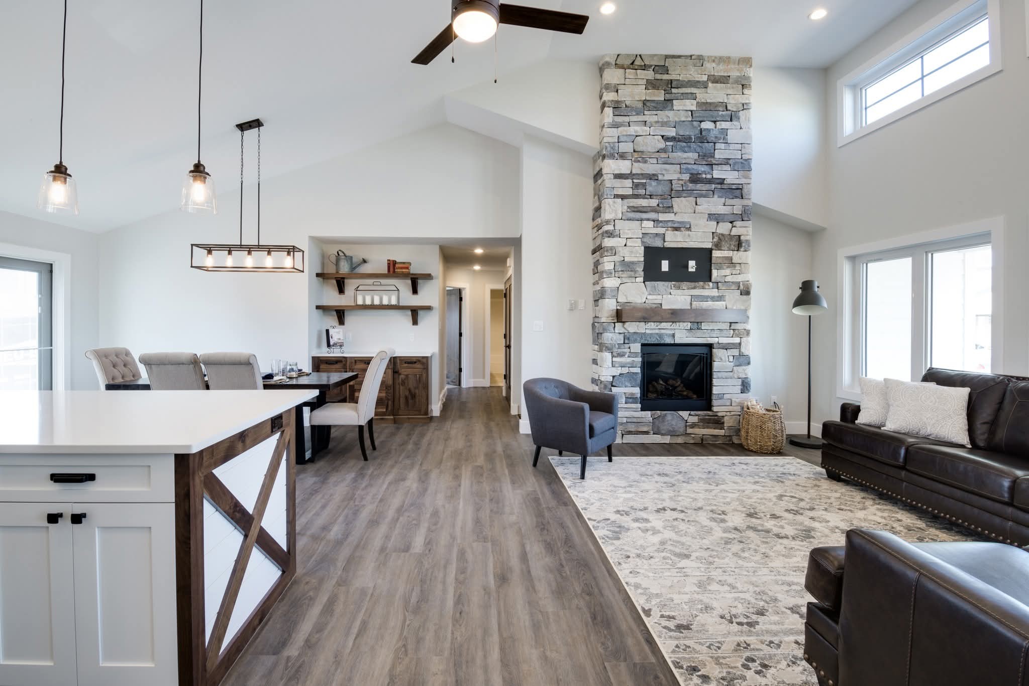 Spacious modern living room with high ceilings, wooden flooring, and stone fireplace. Features elegant lighting, plush sofas, and a cozy, inviting ambiance.