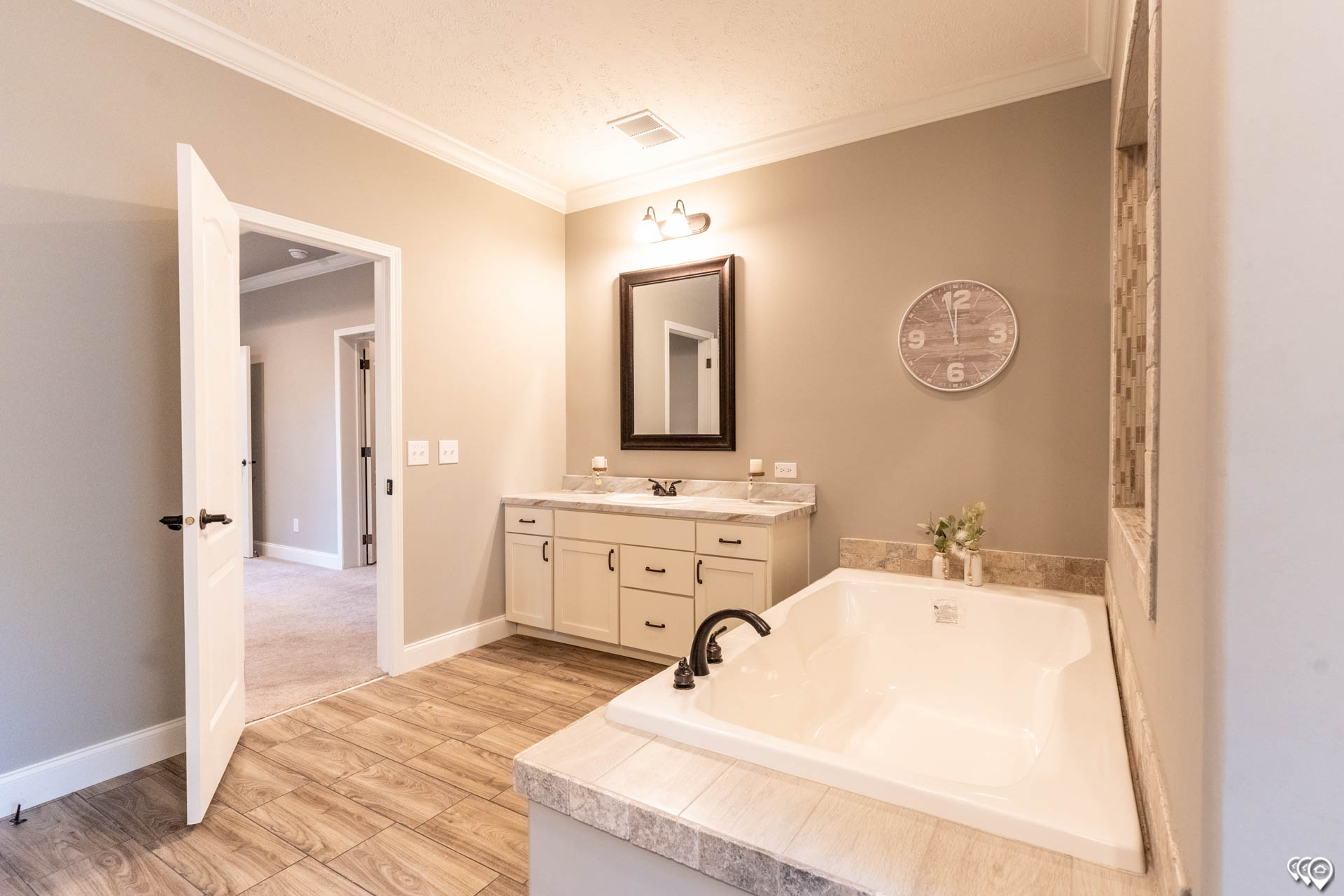 Spacious, modern bathroom with beige walls and wood-look tile flooring. Features a white bathtub, vanity with mirror, and soft lighting for a cozy feel.