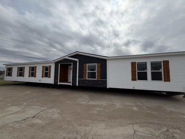 A large modular home with white siding, dark central facade, and wooden shutters under a cloudy sky, conveying a rustic and inviting feel.