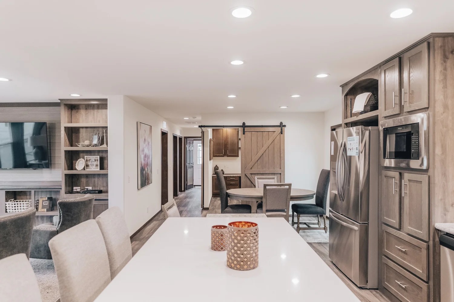 Modern open-concept kitchen and living area. Features a white island with candles, wooden cabinets, stainless steel appliances, and rustic barn door. Cozy and inviting atmosphere.