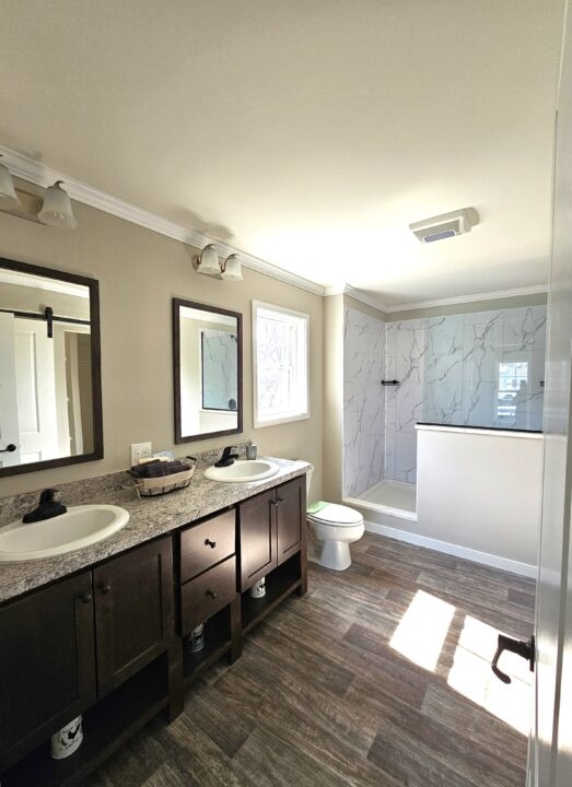 Modern bathroom with dual sinks, dark wood vanity, marble countertops, and a glass walk-in shower. Natural light enhances the bright, clean space.