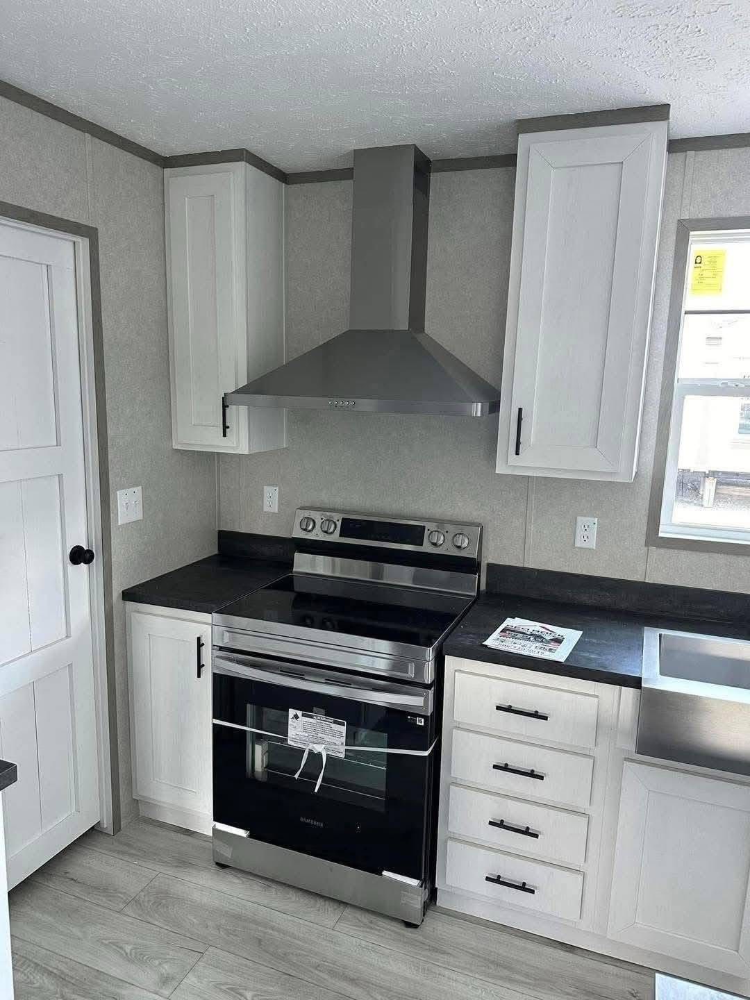 Modern kitchen corner featuring a stainless steel stove with a matching hood, white cabinets, black countertops, and a window, creating a clean, sleek look.