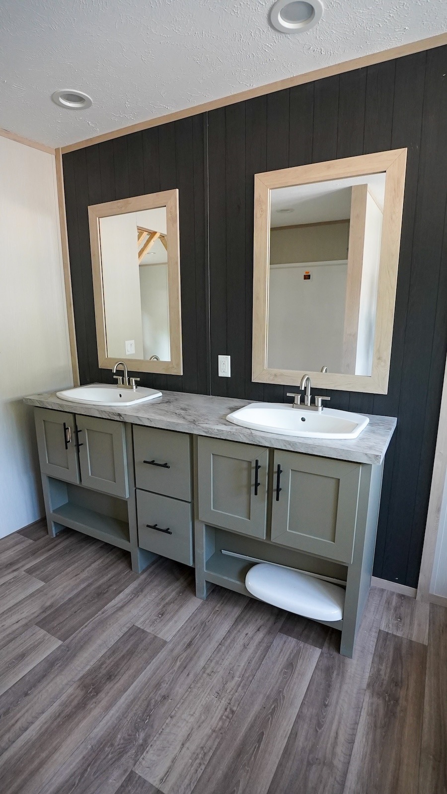 A modern bathroom with two rectangular mirrors above dual sinks on a gray vanity. Dark wood paneling contrasts with the light wood accents and flooring.