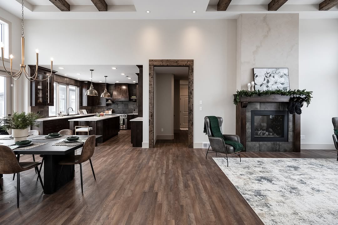 Spacious open-concept living room with wood floors, a modern kitchen, dark cabinetry, a dining table, and a cozy fireplace adorned with greenery.
