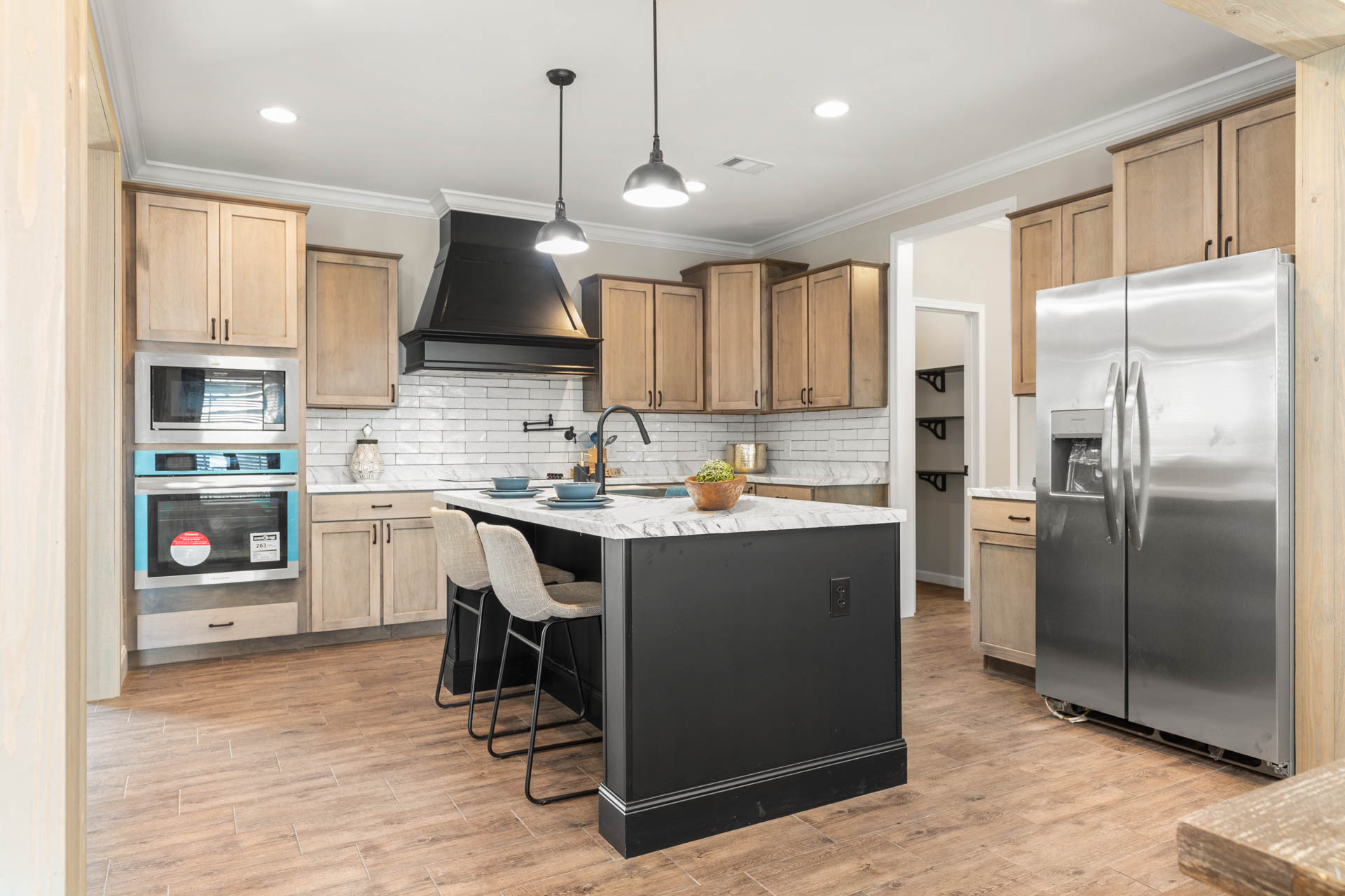 Modern kitchen with light wood cabinets, stainless steel appliances, and a black island. Pendant lights and bar stools create a cozy, elegant atmosphere.