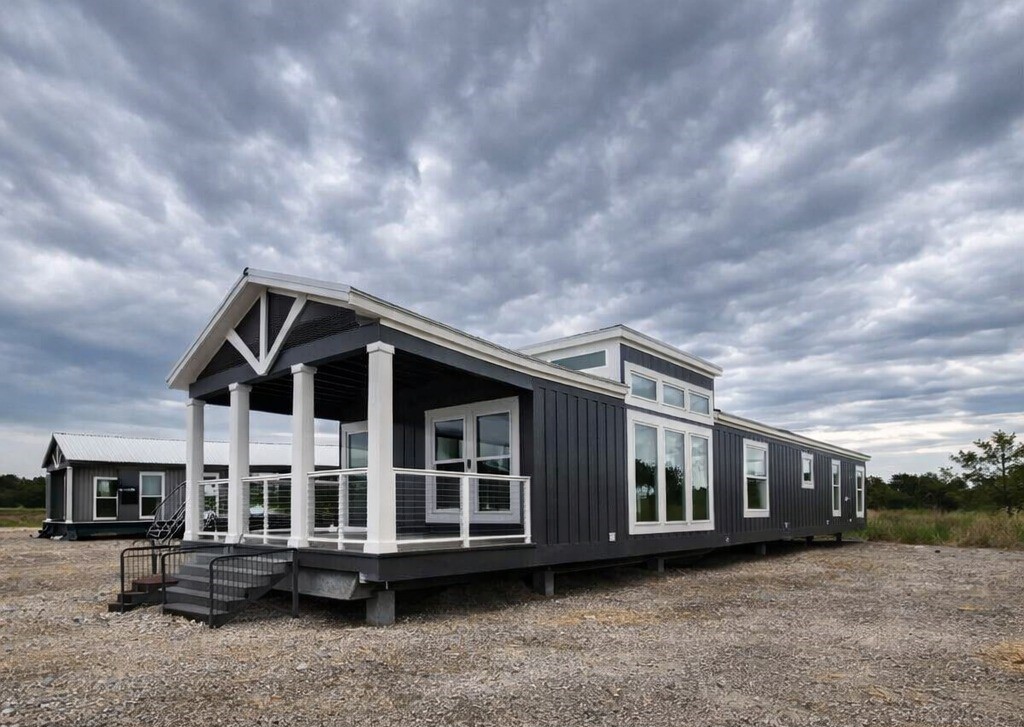 Modern gray modular home with large windows and white trim under a cloudy sky. The home sits on a gravel lot, conveying a sense of simplicity.