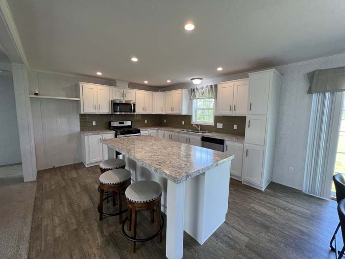 Alt Text: Modern manufactured home kitchen design with white shaker cabinets, dark tile backsplash, and a marble-patterned island countertop.