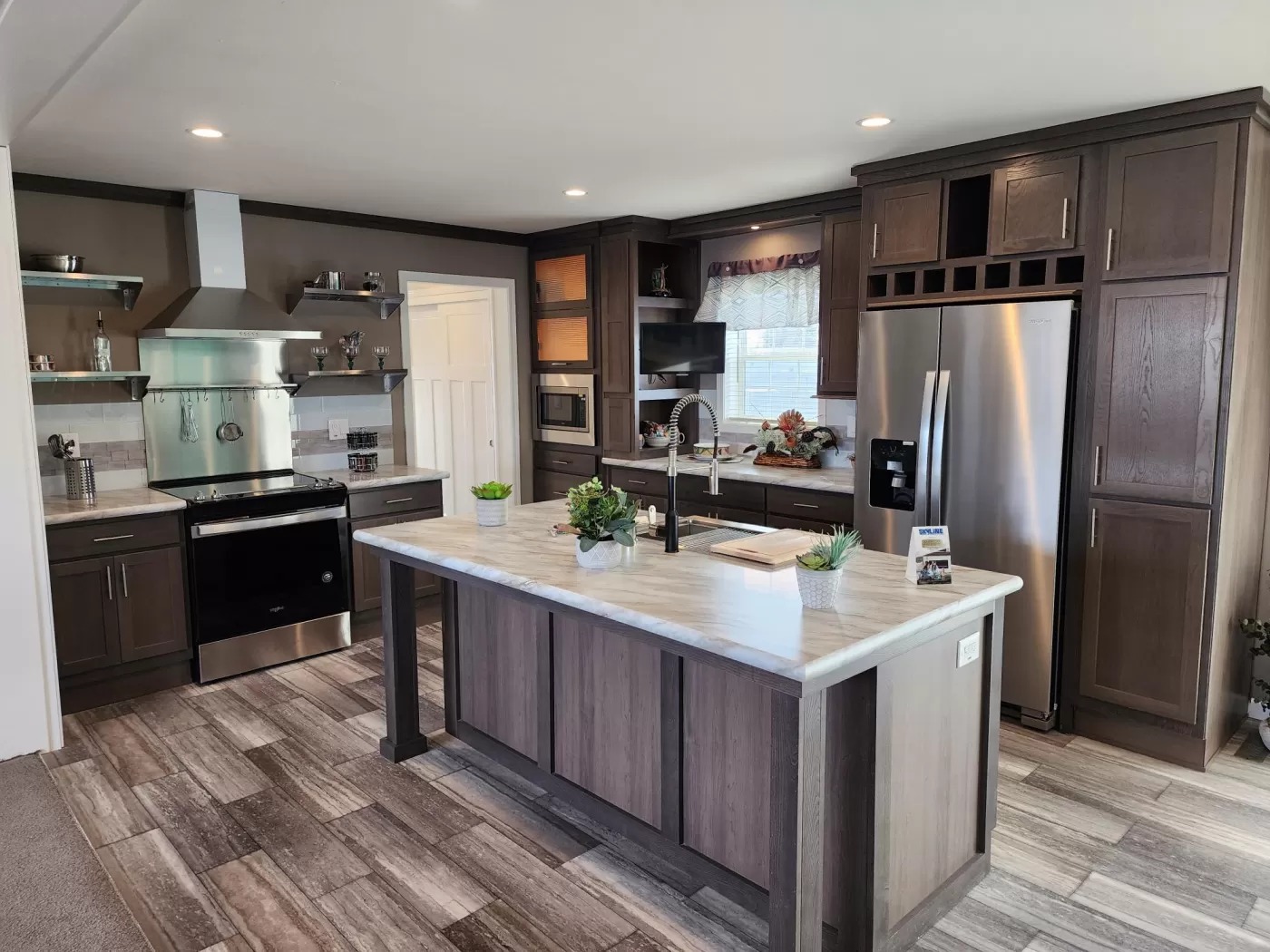 Spacious modern kitchen with wooden cabinets, central island with plants, stainless steel appliances, and recessed lighting, creating a warm and inviting atmosphere.