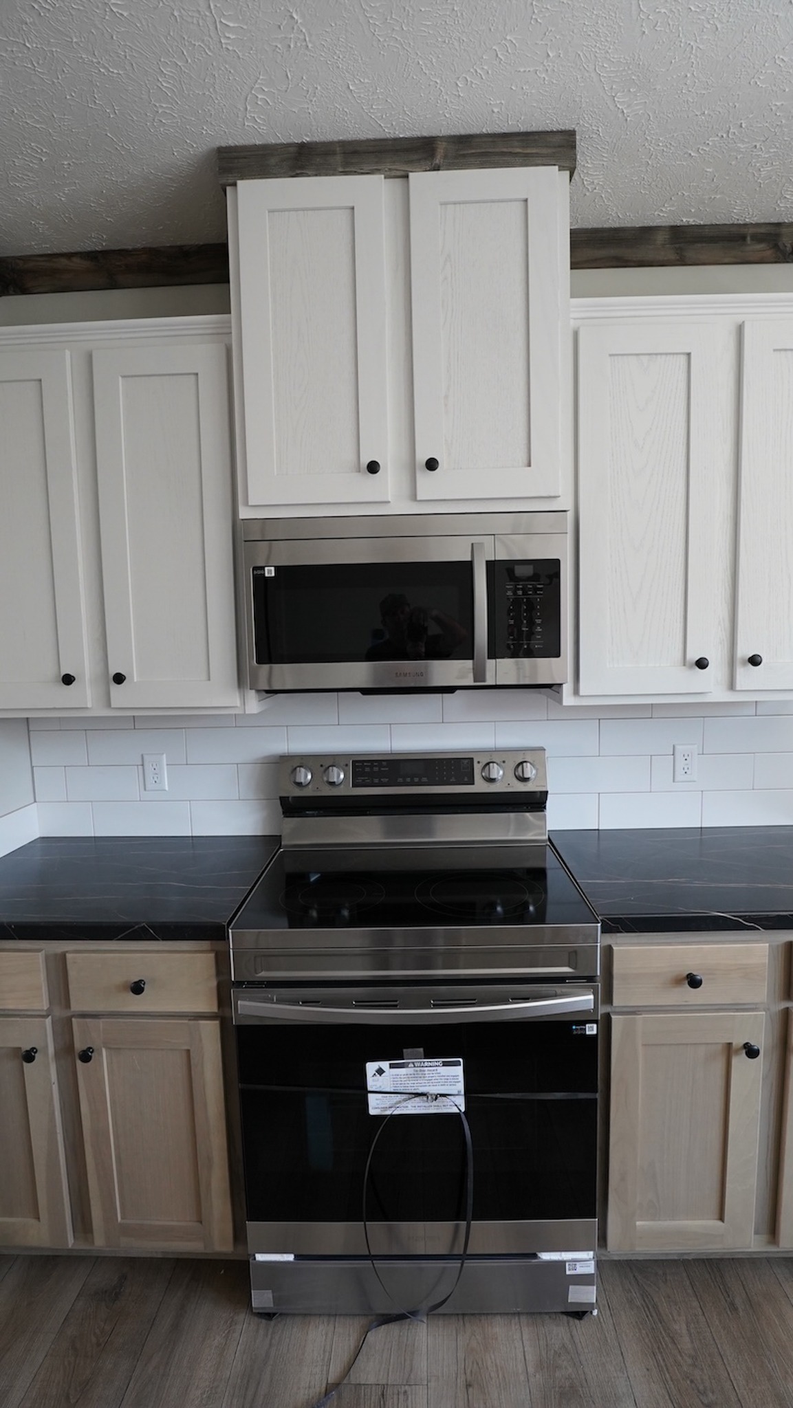 Modern kitchen with white cabinets, stainless steel microwave and oven, black countertops, and light wood flooring, creating a sleek, clean look.