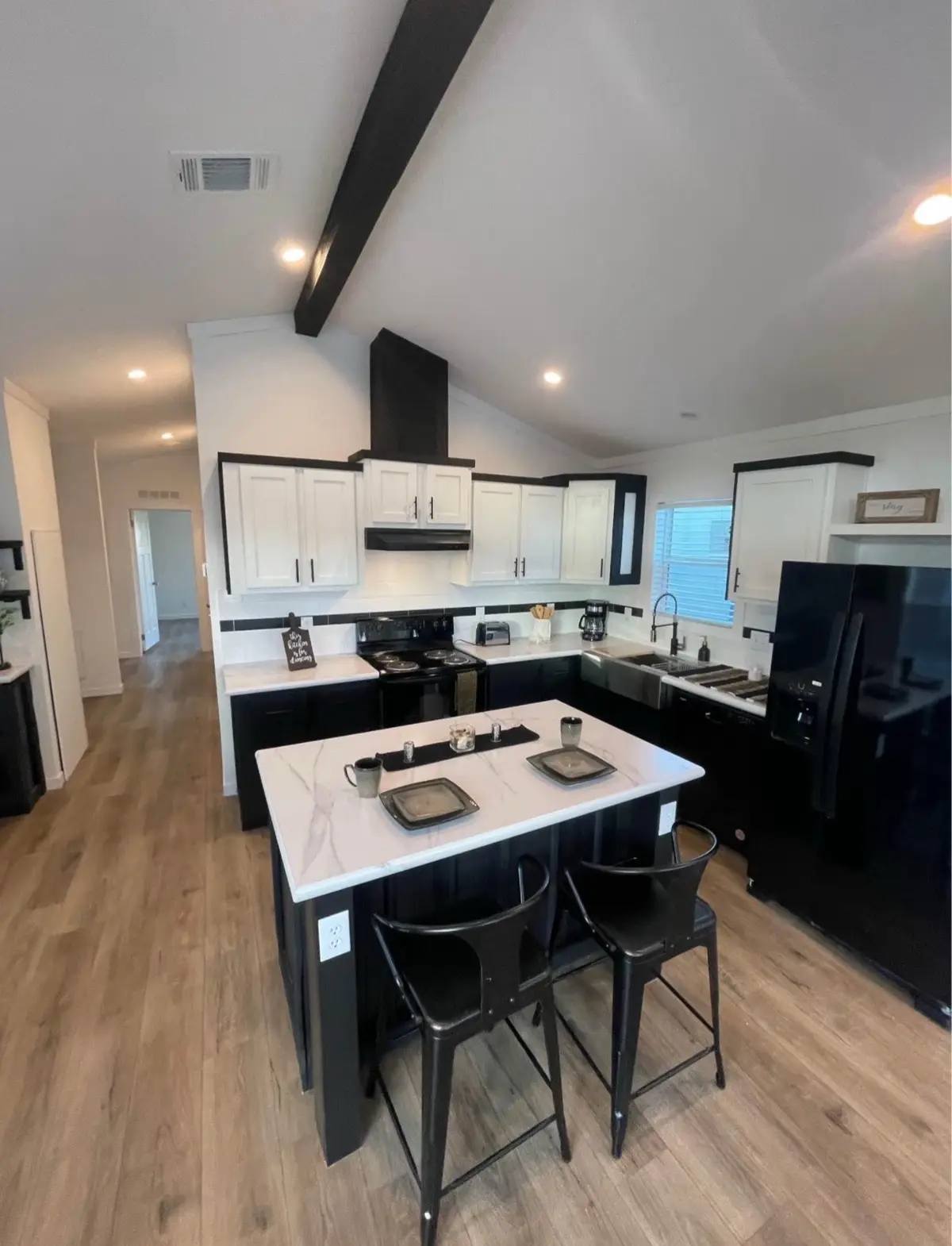 Modern kitchen with vaulted ceiling, featuring black and white cabinets, a central island with two stools, and stainless steel appliances. Cozy and sleek.