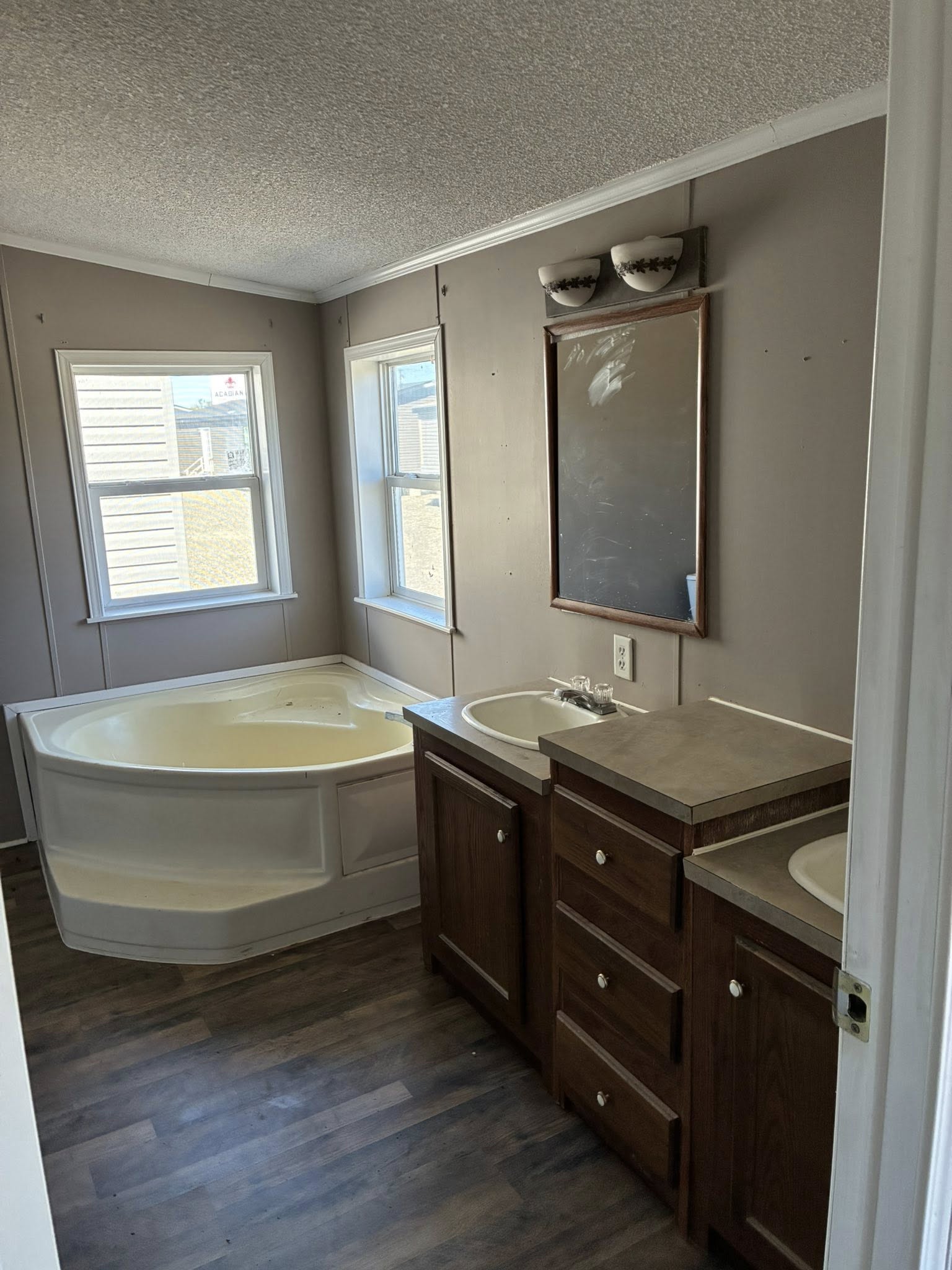 Bathroom with a corner bathtub under two windows, dark wood cabinets, and a large mirror. The room feels clean and simple, with soft natural light.