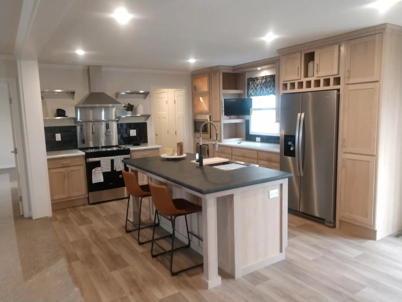 Modern kitchen with wooden cabinets, a large gray island, and orange chairs. Stainless steel appliances and warm lighting create a welcoming tone.