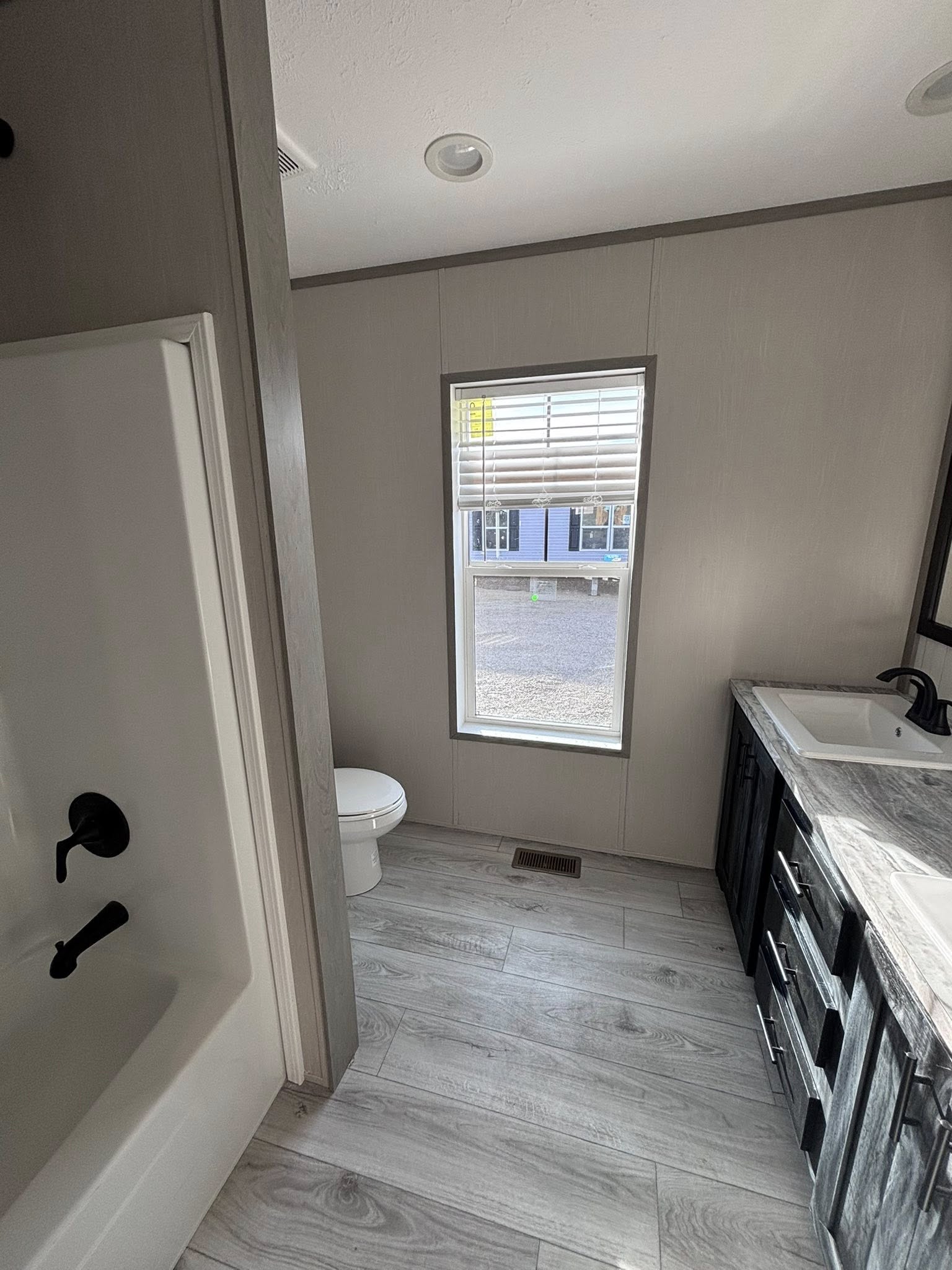 ALT TEXT
A collection of images showcasing the interior of a modern farmhouse-style home with light wood-plank flooring and a neutral color palette. The dining room features a dark wood-top table with white legs, three white chairs, a matching bench, and a large black-and-white forest path canvas on the wall. The kitchen includes a large island with a swirling grey marbled countertop, white cushioned barstools, and a black industrial chandelier with Edison bulbs. Functional kitchen details highlight grey cabinetry, stainless steel appliances, a white farmhouse sink, and a rustic wooden sliding barn door. The final image shows a bathroom with a double vanity featuring a marbled countertop, dark cabinetry, a white toilet, and a white bathtub.