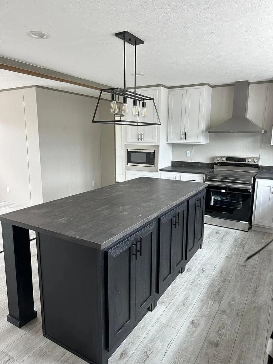 Modern kitchen with black island, light wood floors, and white cabinets. Features a metal pendant light, stainless steel appliances, and a sleek vibe.