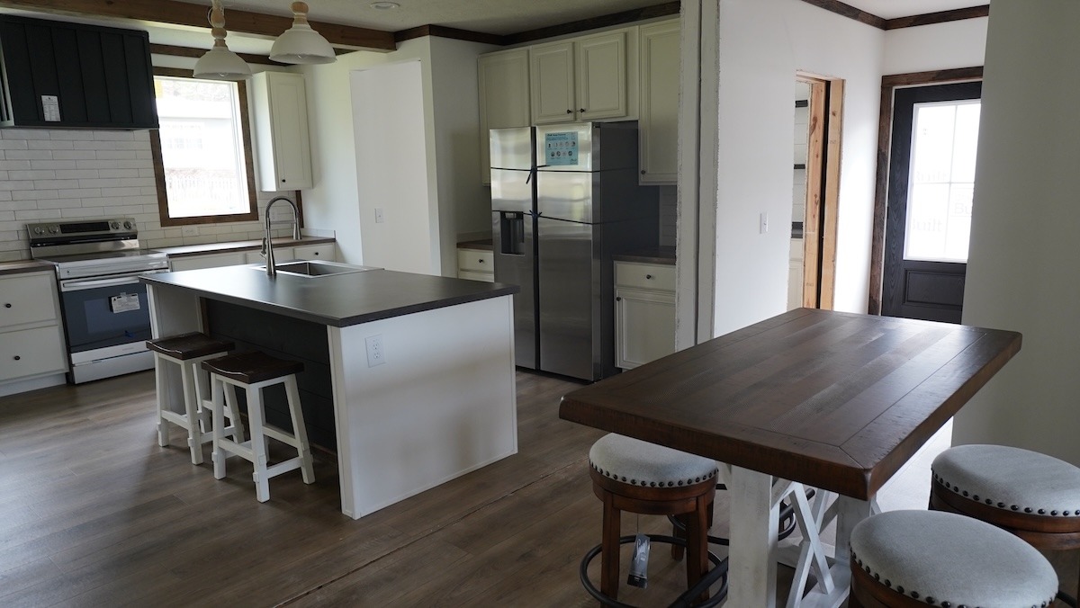 Modern kitchen with light wood flooring, white cabinets, and a stainless steel fridge. Features an island with stools, wooden dining table, and pendant lights, creating a cozy, inviting atmosphere.