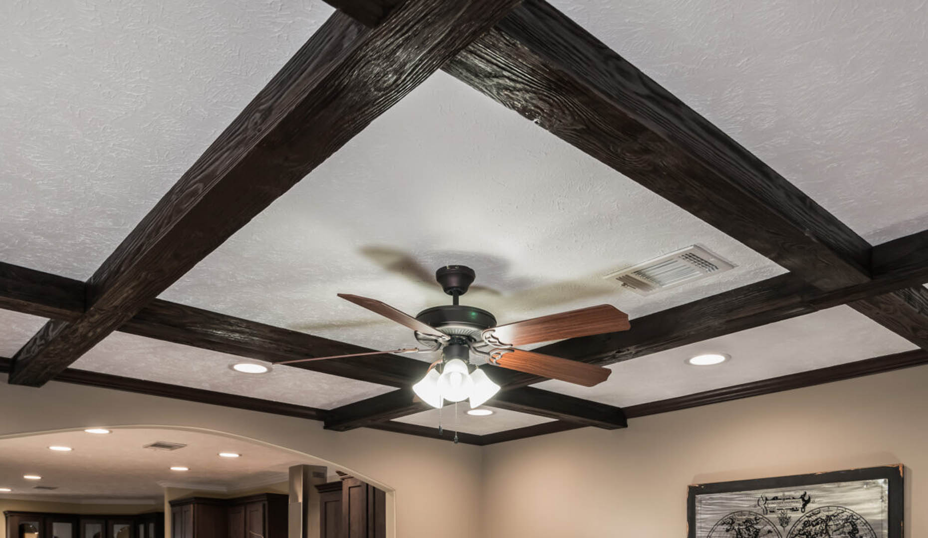 Ceiling with dark wooden beams forming a grid pattern, a central ceiling fan with wooden blades, and recessed lighting, creating a cozy ambiance.