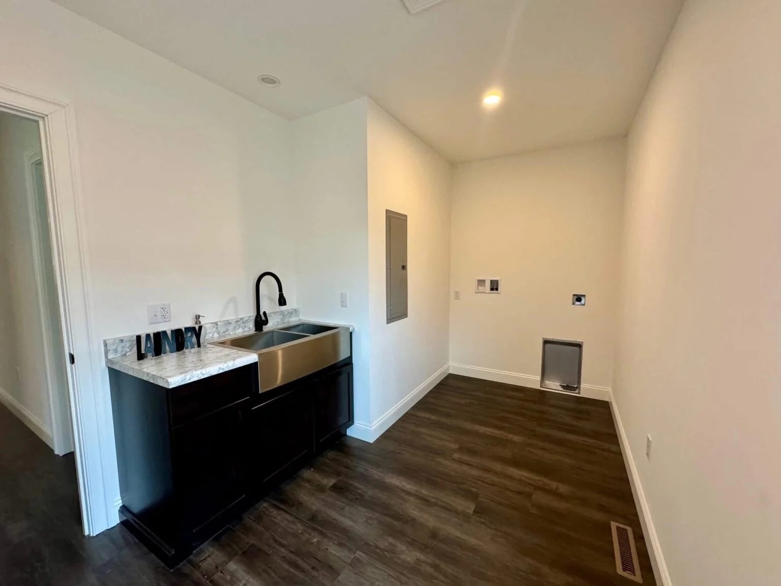 Laundry room with dark wood floors and cream walls. Features a black sink with marble countertop under bright lighting, creating a clean, modern look.