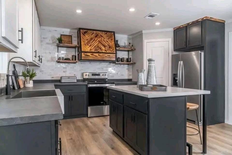 Modern kitchen with dark cabinets and light countertops. Wooden accents on the vent hood and shelving add warmth, while stainless steel appliances enhance a sleek look.