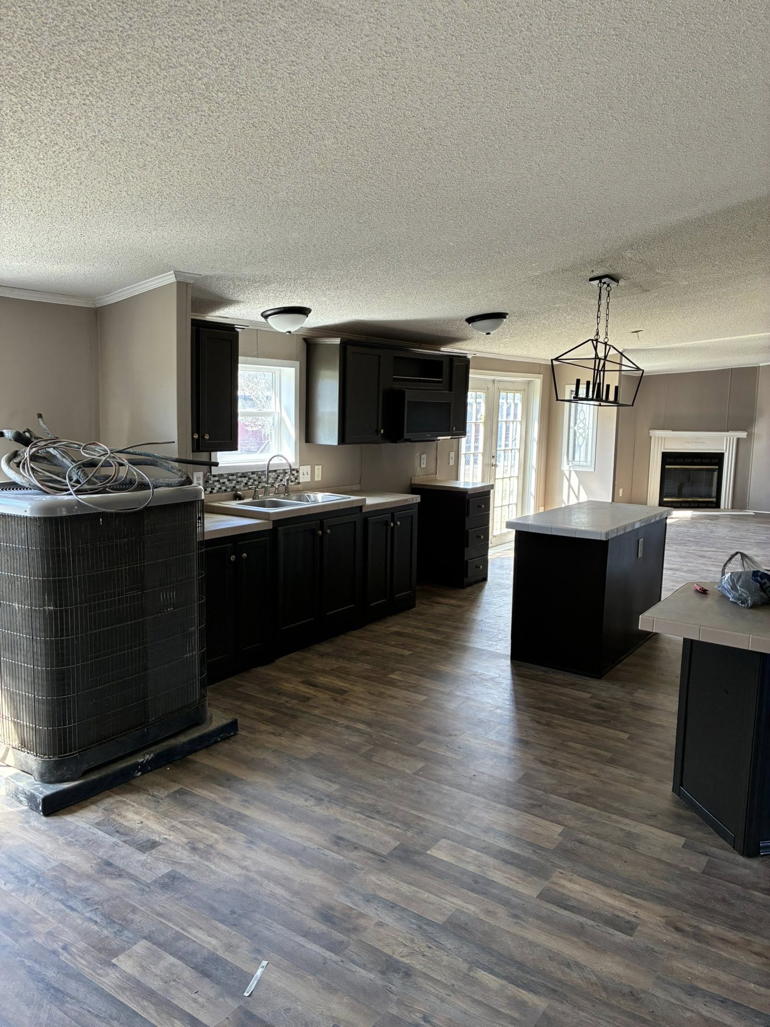 Spacious kitchen with dark cabinets and a central island on hardwood floors. A chandelier hangs above. Sunlight streams through glass doors, creating a cozy ambiance.