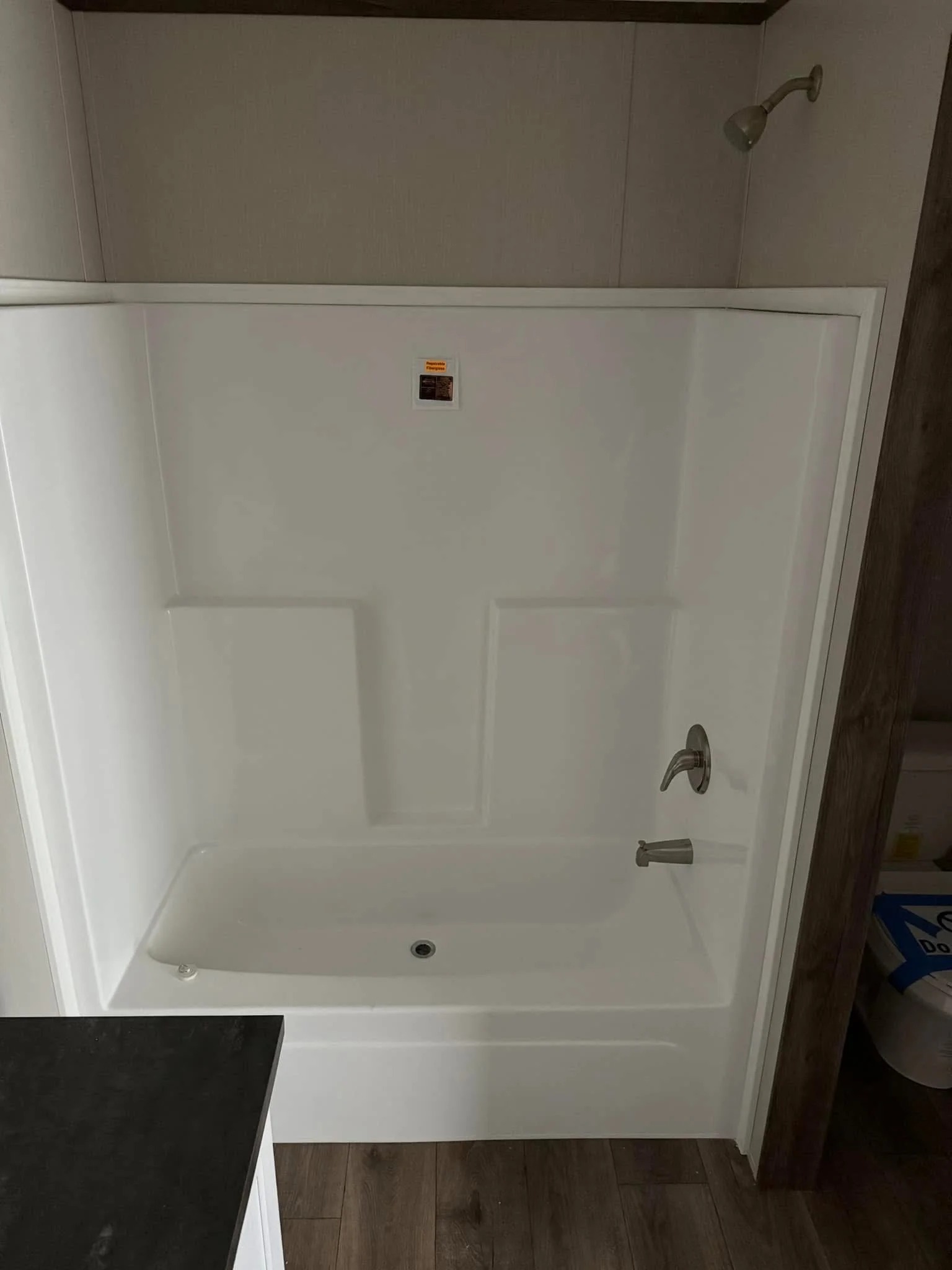 White bathtub with showerhead and faucet against a beige wall. It has a rectangular shape and is installed above a wood-patterned floor. Bright, clean ambiance.