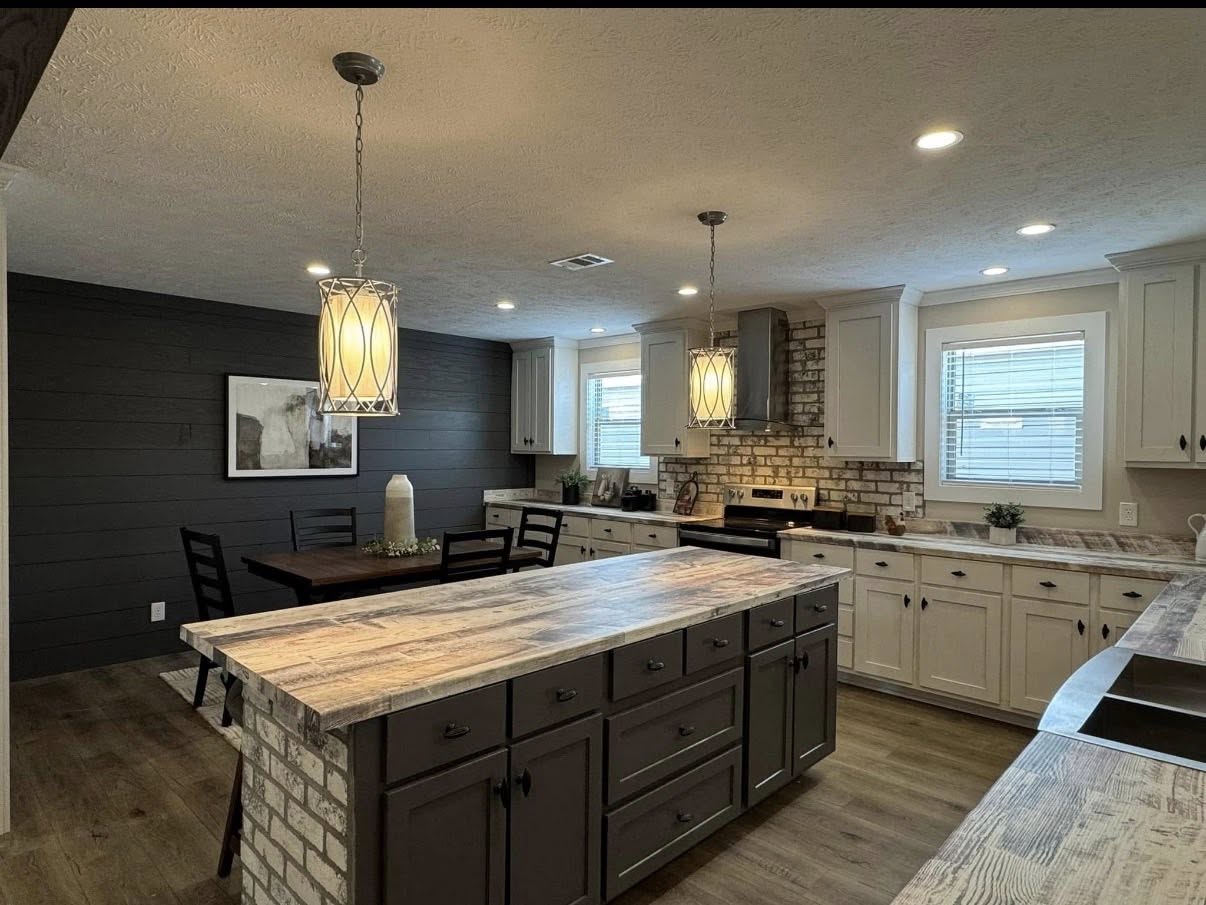 Spacious kitchen with rustic charm, featuring a large island with dark cabinets, wood countertops, and pendant lights. Brick backsplash and cozy dining area.