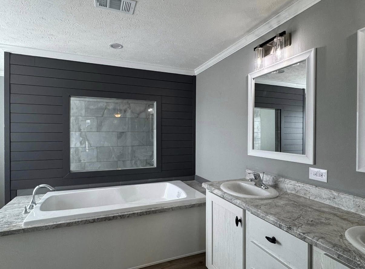 Modern bathroom with a gray bathtub under a dark shiplap wall. It features a marble countertop with two sinks and framed mirrors above.