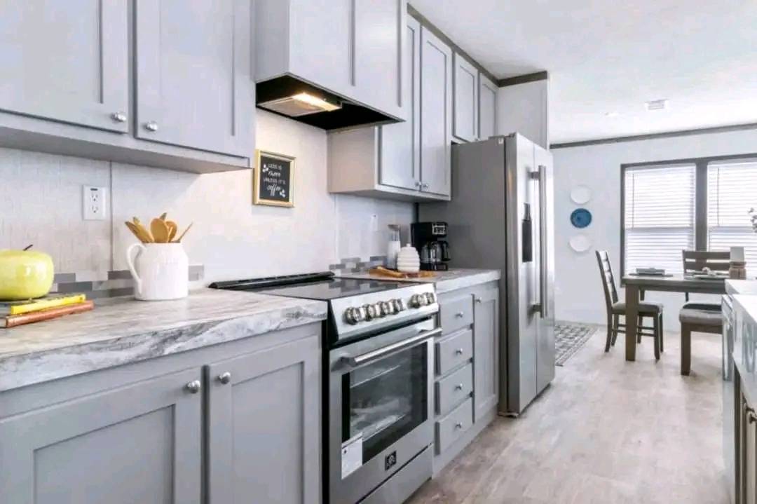 Modern kitchen with gray cabinets, marble countertop, stainless steel appliances, and a dining table in a bright room. A cozy and inviting atmosphere.