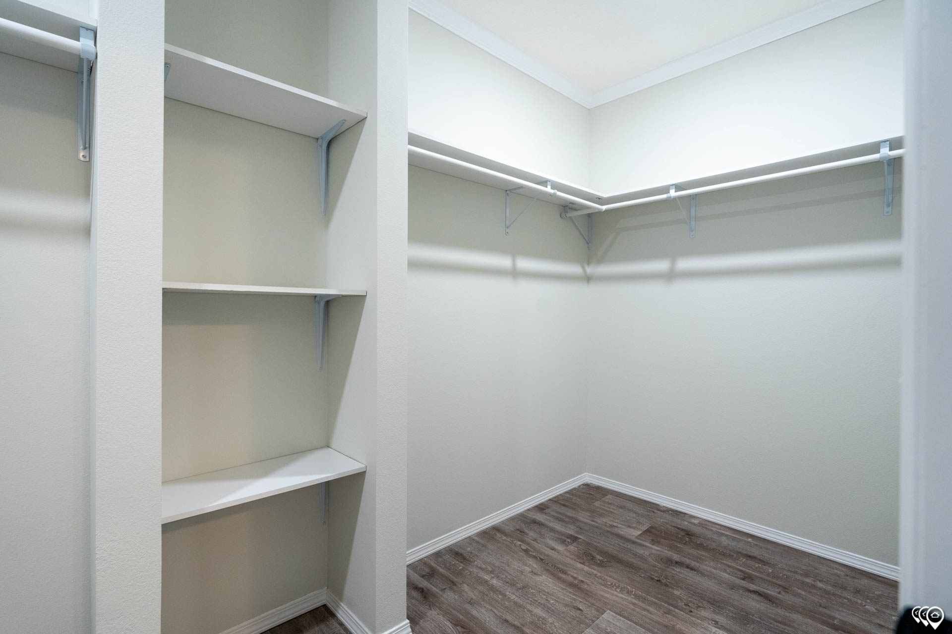 Spacious, empty walk-in closet with open shelves on the left, railings on the right, and hardwood floors. The ambiance is clean and minimalistic.