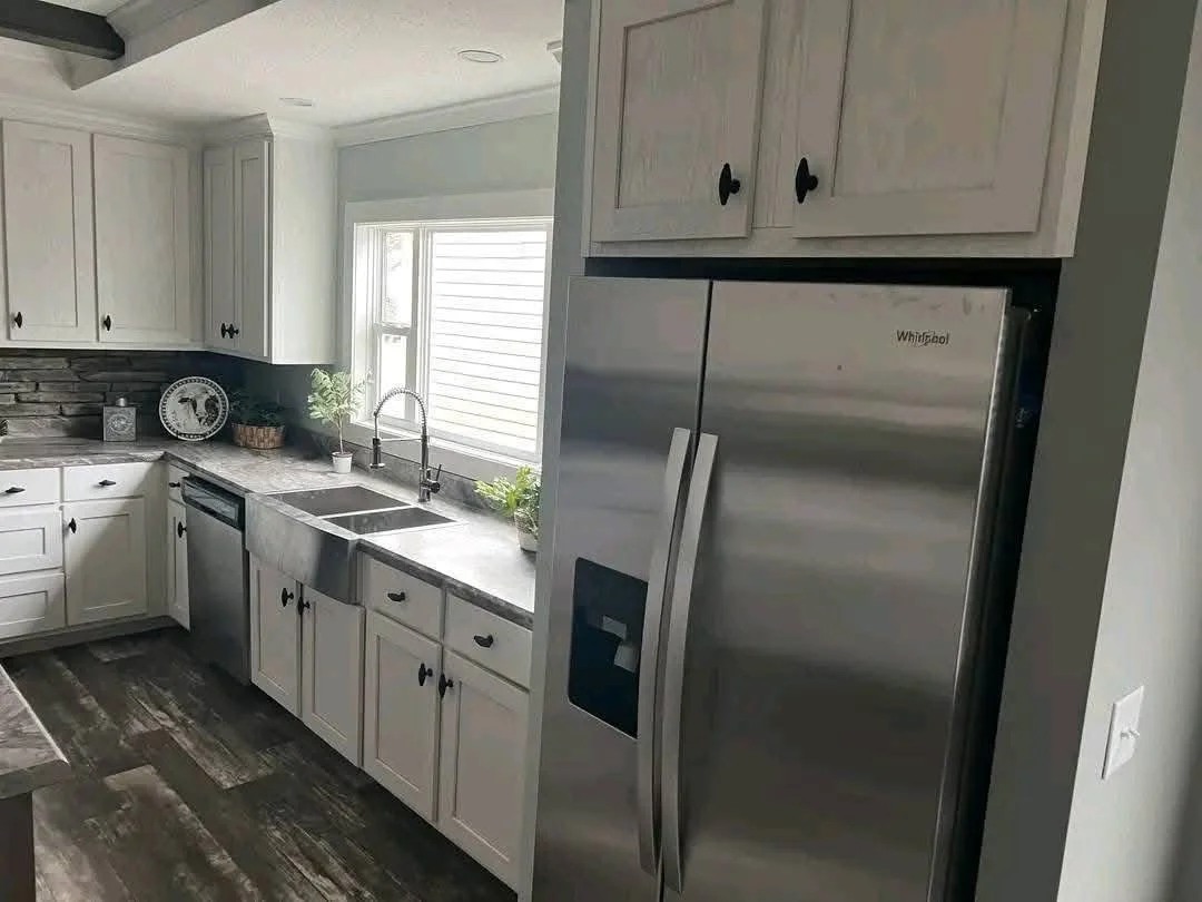 Modern kitchen featuring stainless steel fridge, white cabinets, dark countertops, and stone backsplash. Bright, inviting atmosphere with natural light.