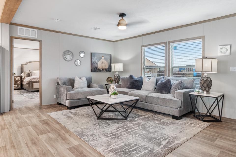 A modern living room with gray sofas, a geometric coffee table, and a large rug. Soft lighting emits a cozy ambiance, with artwork and decor on walls.