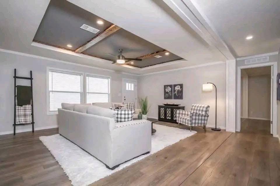 Spacious living room with light gray walls, wood flooring, and modern recessed ceiling. Features a gray sofa, two plaid armchairs, and standing lamp.
