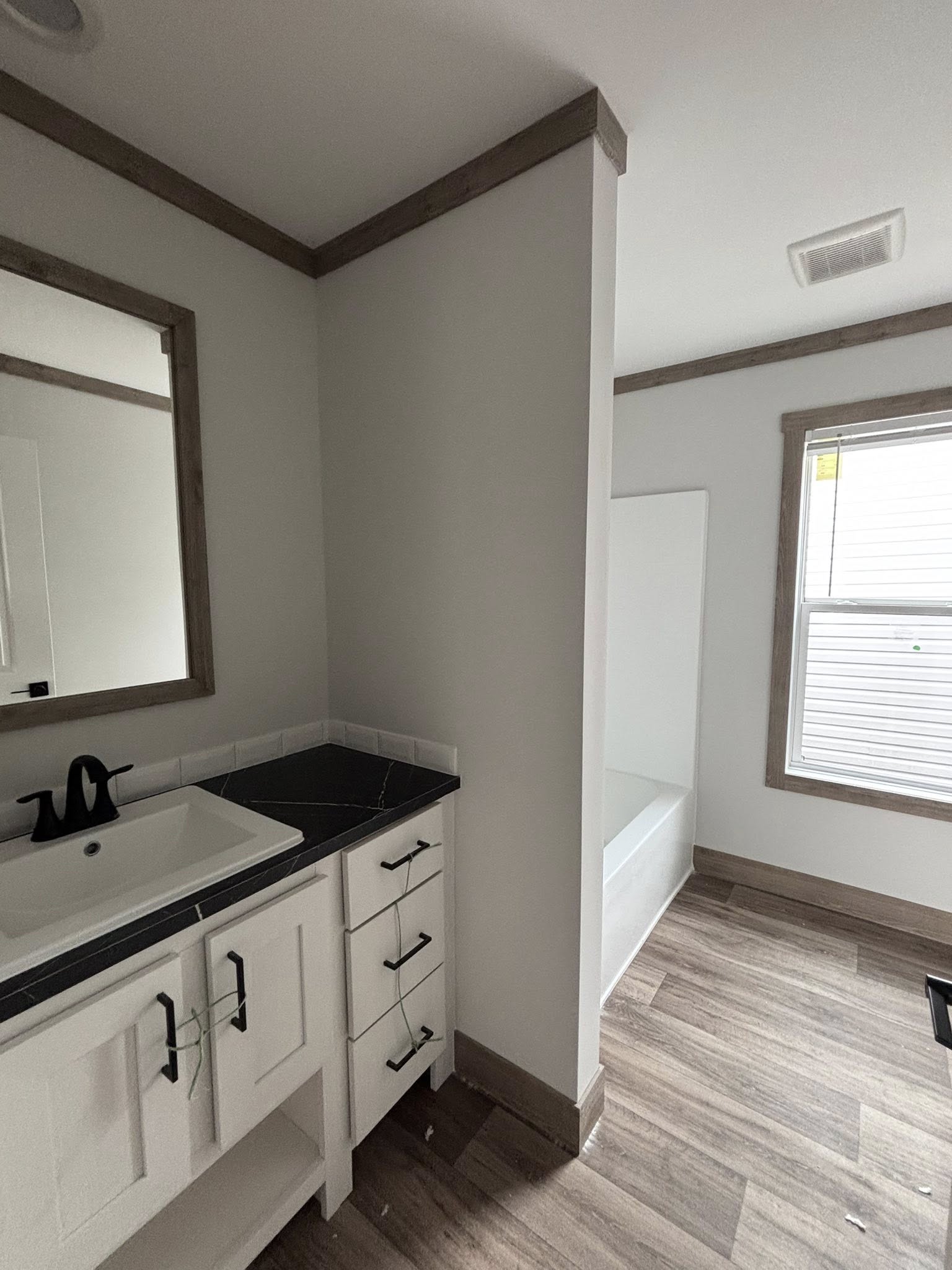 This extensive image gallery showcases the "Boujee XL" series of luxury tiny homes and manufactured residences, featuring a refined modern farmhouse aesthetic through high-end exterior and interior finishes. Exterior designs highlight high-contrast palettes, such as white or cream board-and-batten siding paired with dark charcoal gables, gabled front porches with black or white support pillars, and durable metal roofs. Interior living areas emphasize open-concept luxury with vaulted ceilings—some featuring natural wood planks, exposed beams, or industrial-style ceiling fans—complemented by wide-plank wood-look flooring and crisp shiplap or neutral walls. Gourmet kitchens are equipped with premium features, including cabinetry in natural oak, white, or black finishes, marble-patterned or wood-block countertops, stainless steel farmhouse sinks, and large center islands with modern pendant lighting. Additional functional luxury elements include integrated loft spaces, transom windows for maximum natural light, built-in breakfast booths, and contemporary bathrooms with black hardware and white vanities.