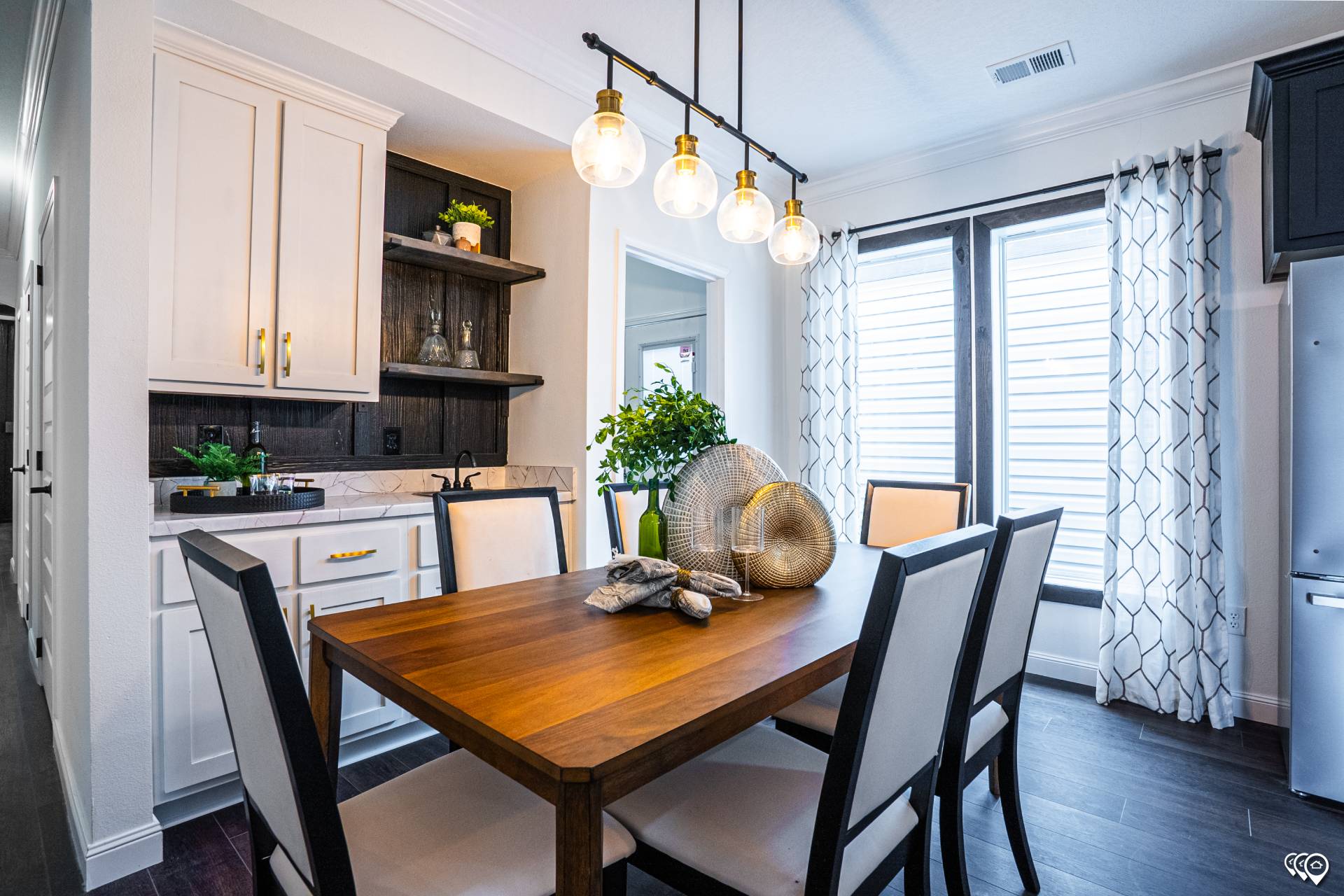 Modern dining room with a wooden table, six white chairs, and a statement pendant light. Large windows with sheer curtains add brightness.