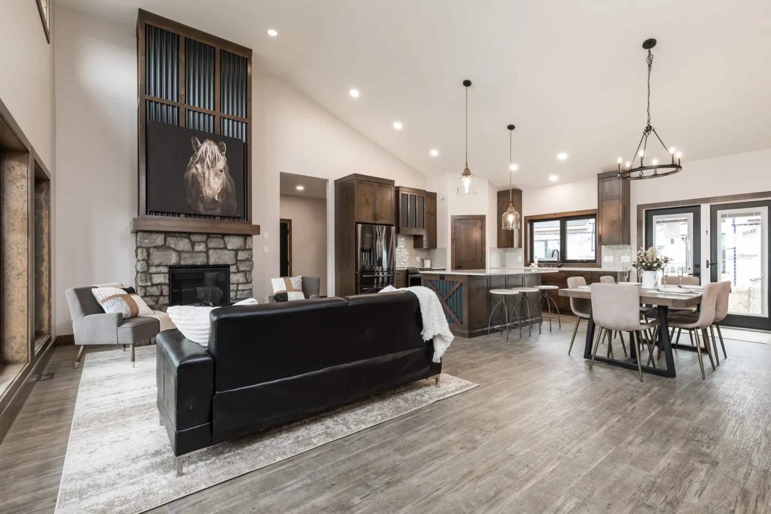 Spacious open-plan living room and kitchen with wooden flooring, featuring a black sofa, stone fireplace, lion artwork, and a modern dining area with soft lighting.