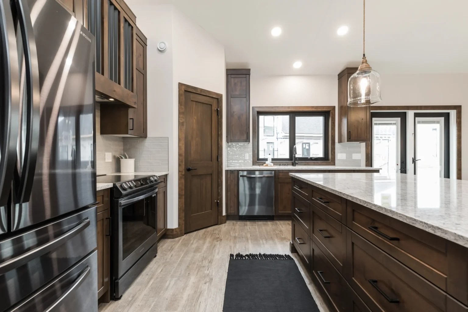 Sleek kitchen with dark wooden cabinets, stainless steel appliances, large island with granite countertop, and pendant lighting. Bright, modern, and spacious tone.