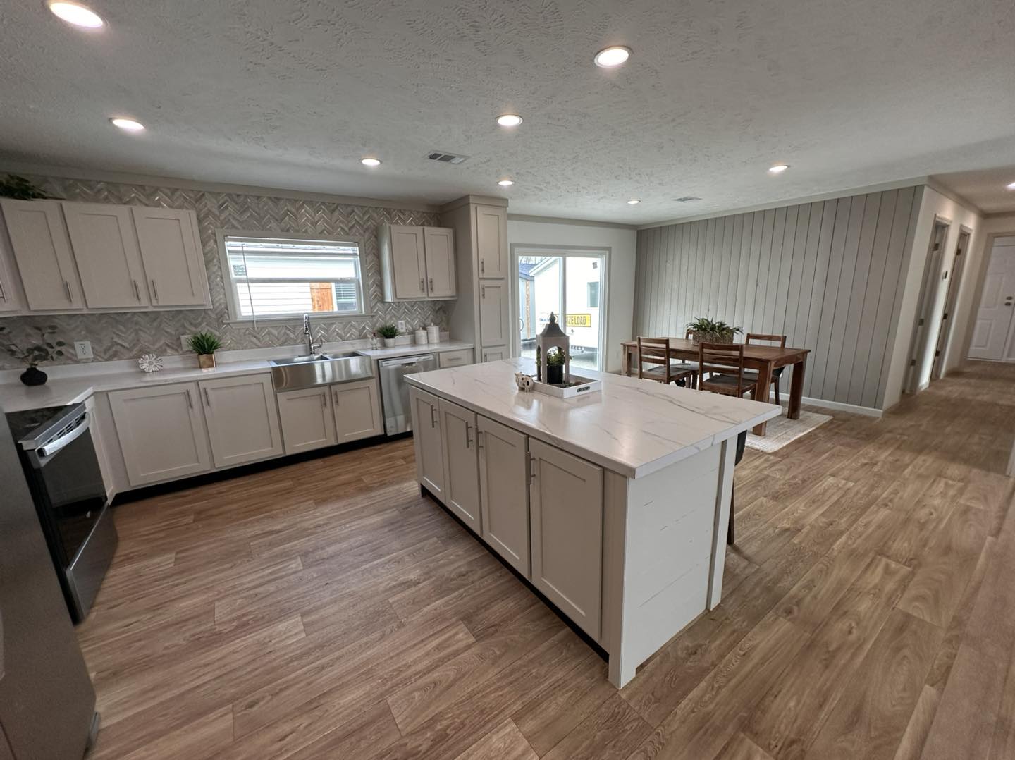 Luxury modern modular home showcase featuring the APH 1662C 819 SQ FT show home and expansive double-wide models, with white vertical board and batten siding, dark charcoal horizontal siding with rustic wood shutters, and luxury interiors featuring vaulted shiplap ceilings with dark wood beams, gourmet kitchens with marble-look waterfall islands and custom pull-out pantry storage, open-concept living rooms with integrated electric fireplaces and shiplap accent walls, cozy bedrooms with modern white iron or tufted bed frames, and a spacious covered front porch with a dark wood-plank ceiling and stylish hanging wicker egg chair.