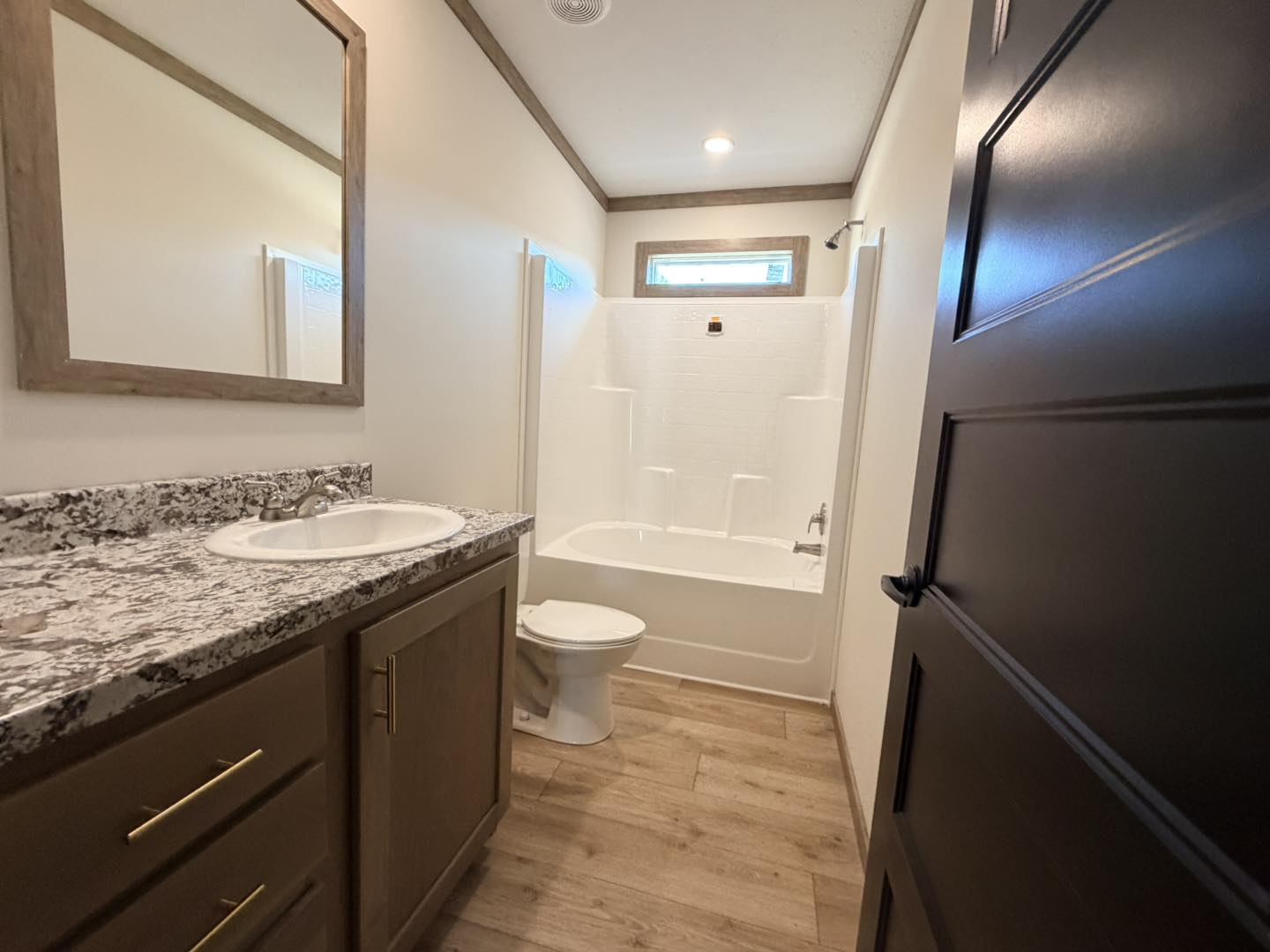 Modern bathroom with wood-textured floor, granite countertop with sink, and a white bathtub. Soft lighting creates a clean, inviting feel.