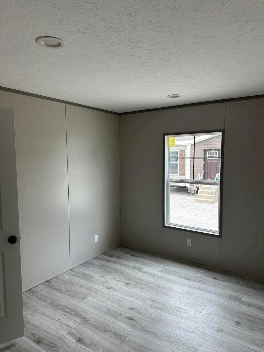Empty room with light gray walls and wood-patterned floor. A window on the right overlooks a yard with a building. Minimalist, neutral, and calm.