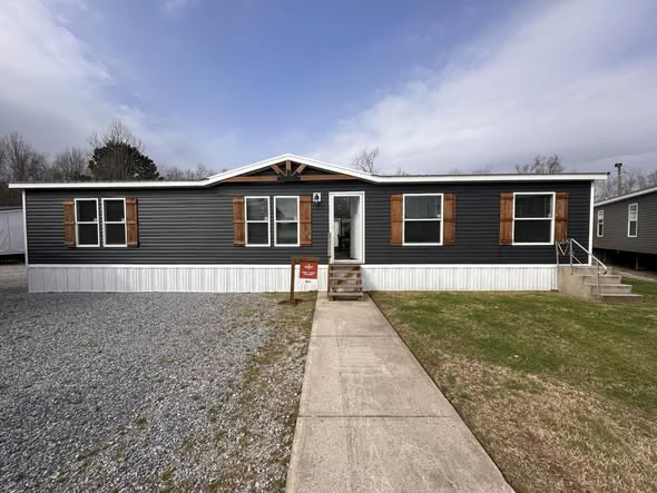 Modern modular farmhouse showcase featuring the APH 1662C 819 SQ FT show home with white vertical board and batten siding, luxury interiors with a floor-to-ceiling stacked stone fireplace, vaulted shiplap ceilings with dark wood beams, a gourmet kitchen with a granite waterfall island and black industrial pendants, custom pantry with pull-out wooden drawers, cozy bedrooms with dark-trimmed windows, and a spacious covered front porch with a wood-plank ceiling and hanging egg chair.