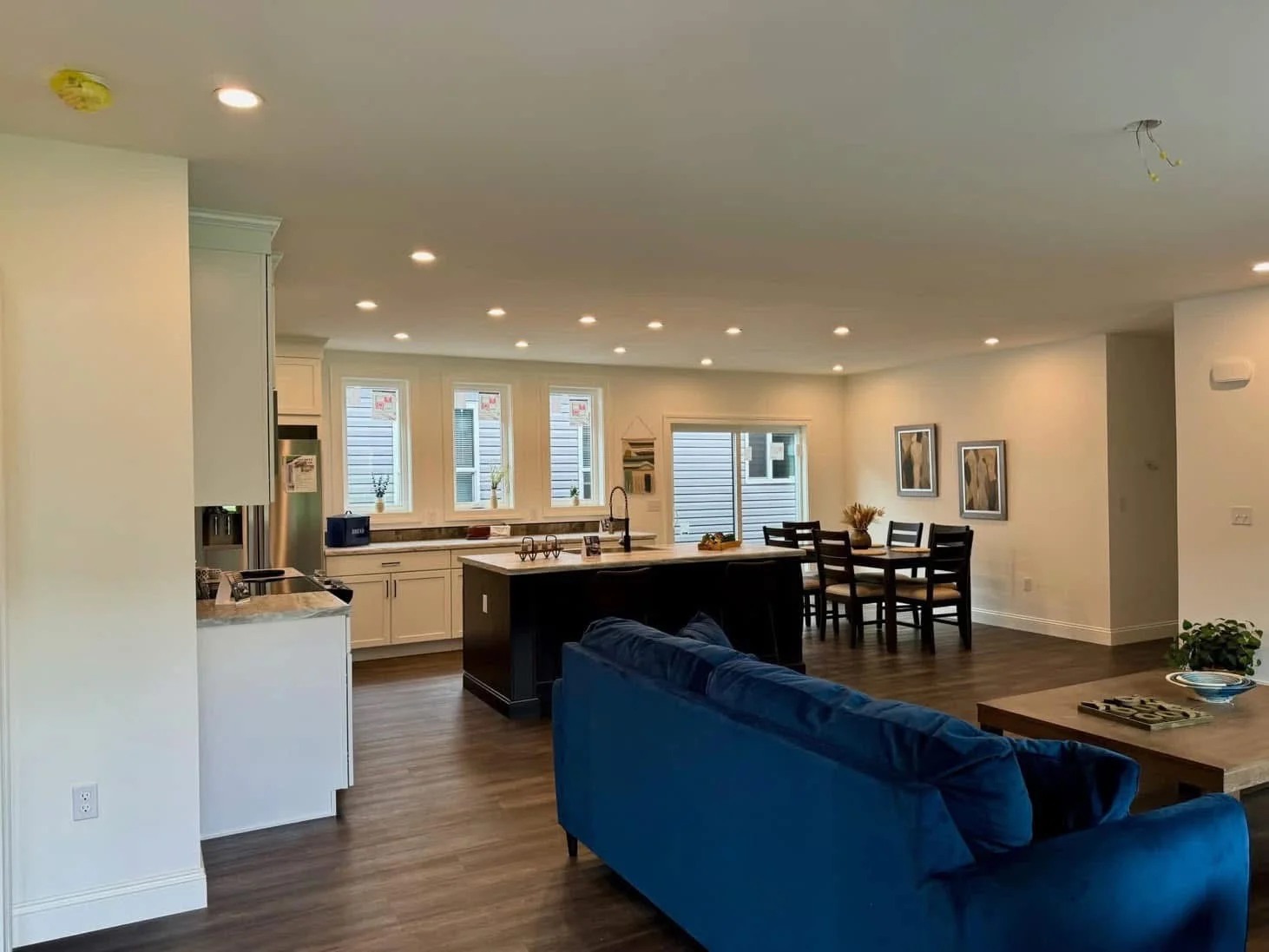 Spacious open-plan kitchen and dining area with hardwood floors. Blue sofa, modern fixtures, white cabinets, island with sink, and dining table.