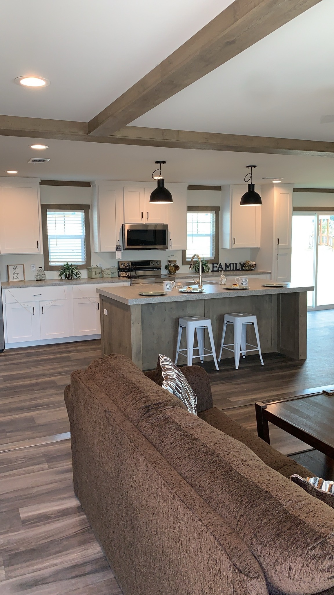 Luxury manufactured and modular home collection featuring an 819 SQ FT farmhouse floor plan, modern white kitchens with quartz waterfall islands, hidden arched pantries, industrial-style corrugated metal accents, and rustic-modern living spaces with stone fireplaces and sliding barn doors.