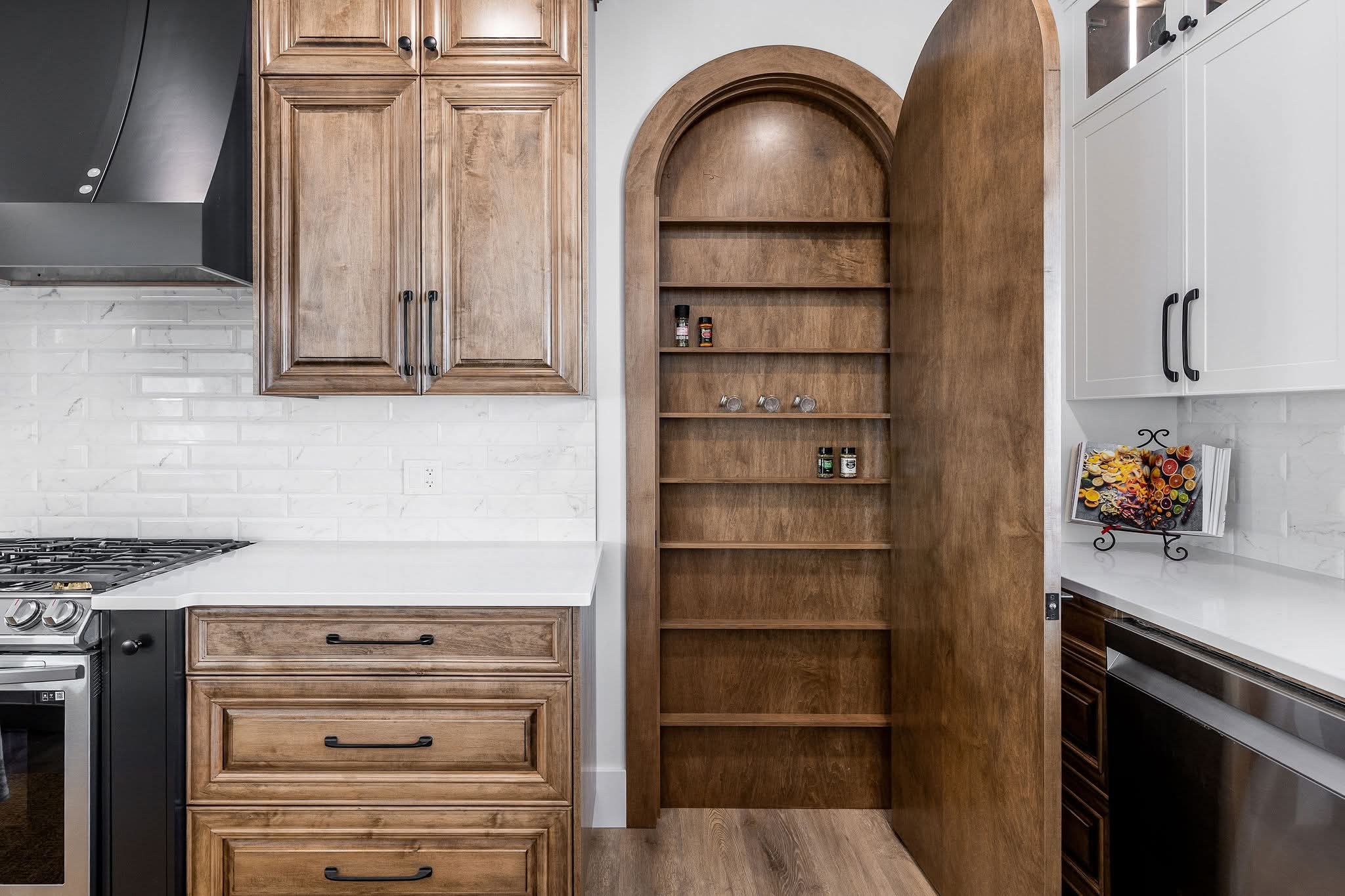 Wooden pantry door disguised as a shelf, open within a modern kitchen. Features white countertops, wooden cabinetry, and a gas stove. Cozy mood.