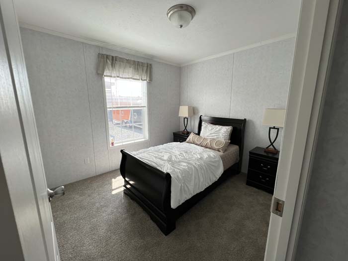 Cozy manufactured home guest bedroom featuring a dark wood sleigh bed, white bedding, and large windows.