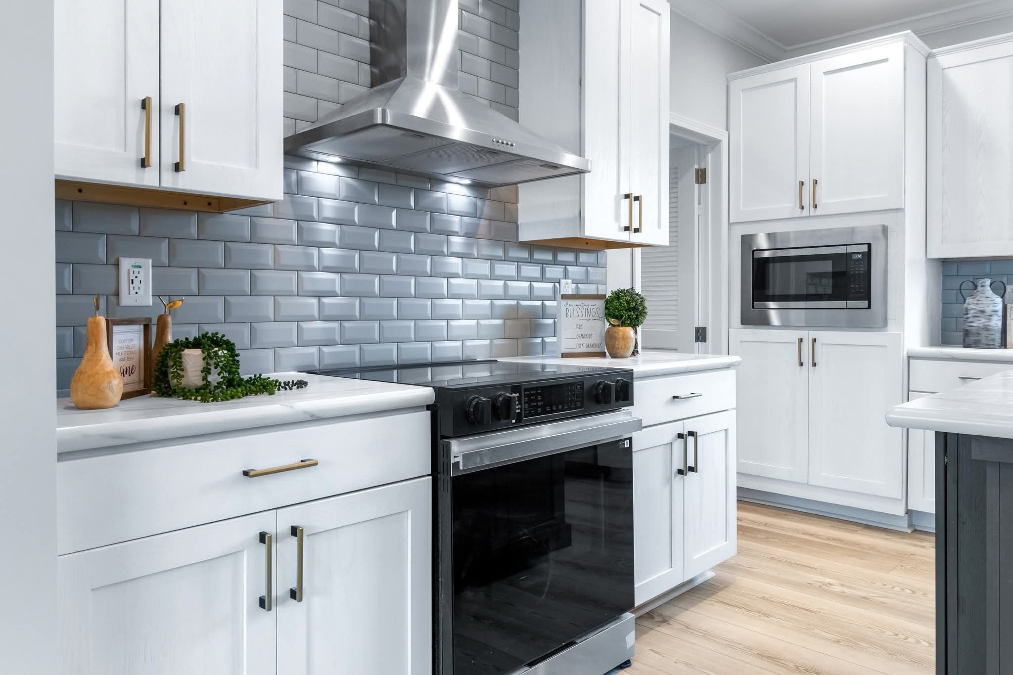 Modern kitchen with white cabinets and a stainless-steel stove. Glossy subway tiles and light wood flooring create a clean, minimalist vibe.