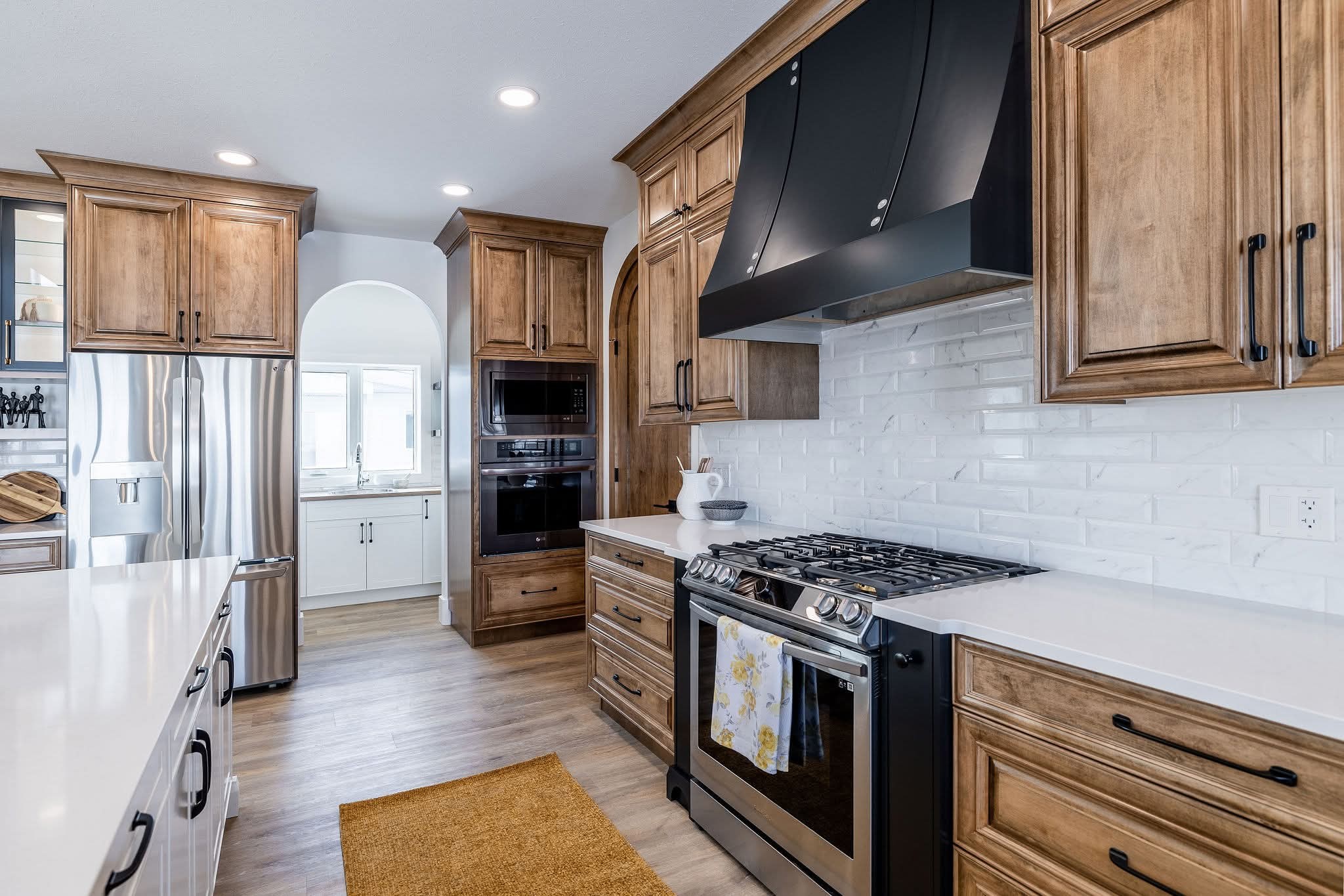 Modern kitchen with wooden cabinets, stainless steel appliances, white countertops, and a black range hood. Bright and spacious with elegant design.