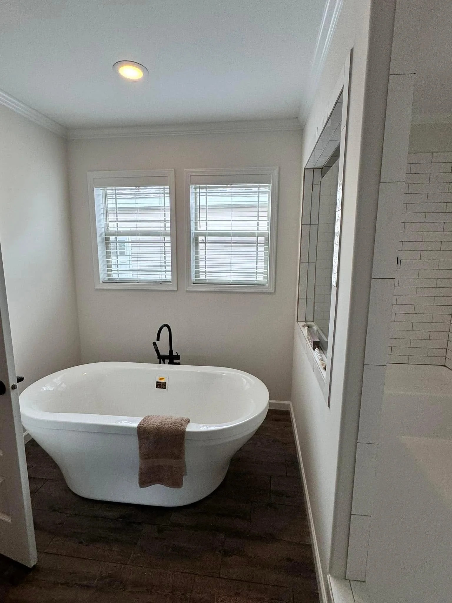 Stylish bathroom with a white freestanding bathtub, black faucet, and a towel draped over the side. Dual windows and wooden floor add elegance.